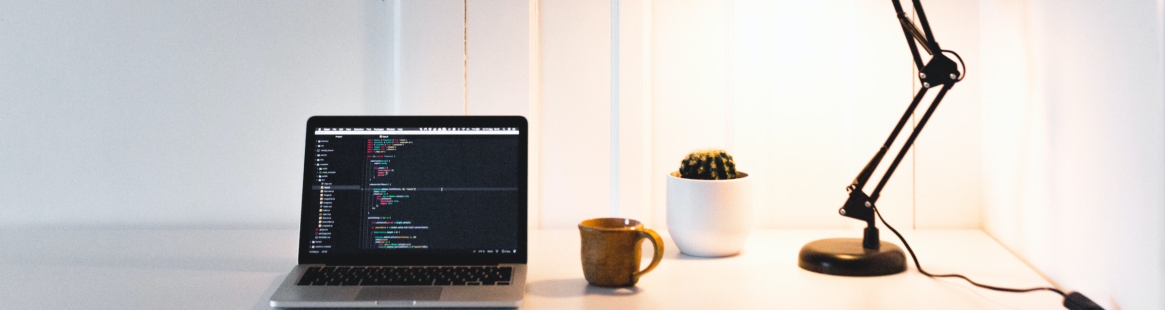 a desk with developer's laptop showing code with a mug and a lamp on the side